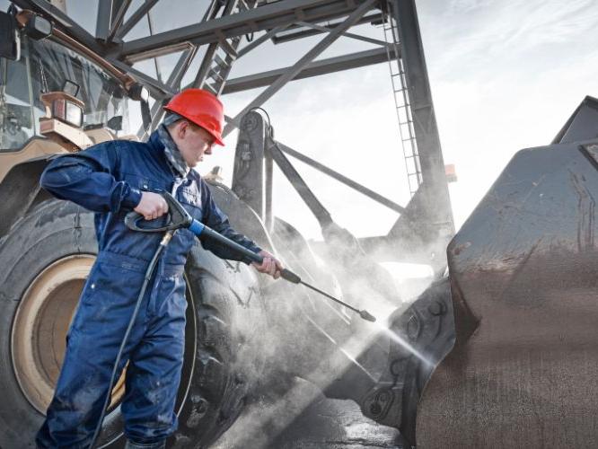 Worker using a high-pressure cleaner to wash equipment at a mining or industrial worksite.
