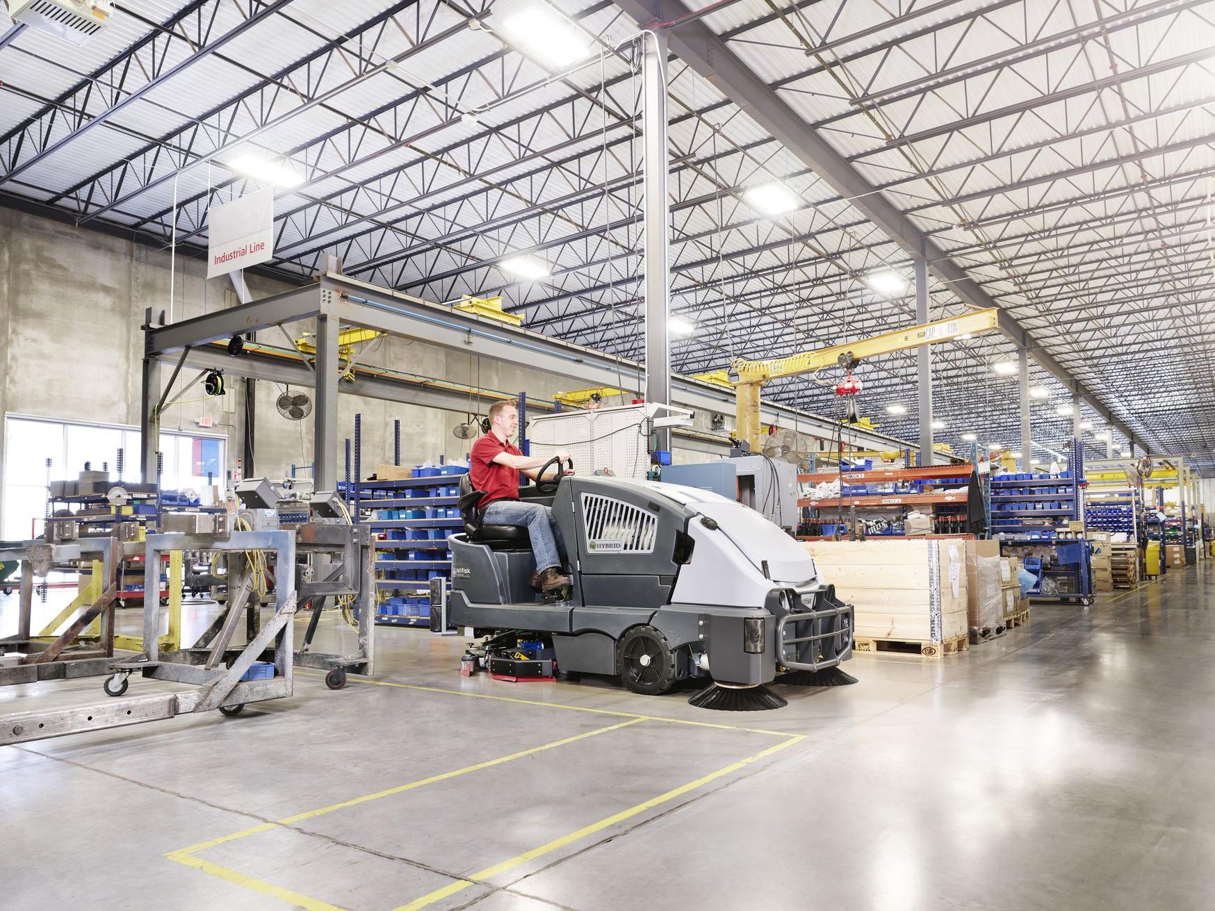 Industrial floor scrubber cleaning a large manufacturing warehouse floor.