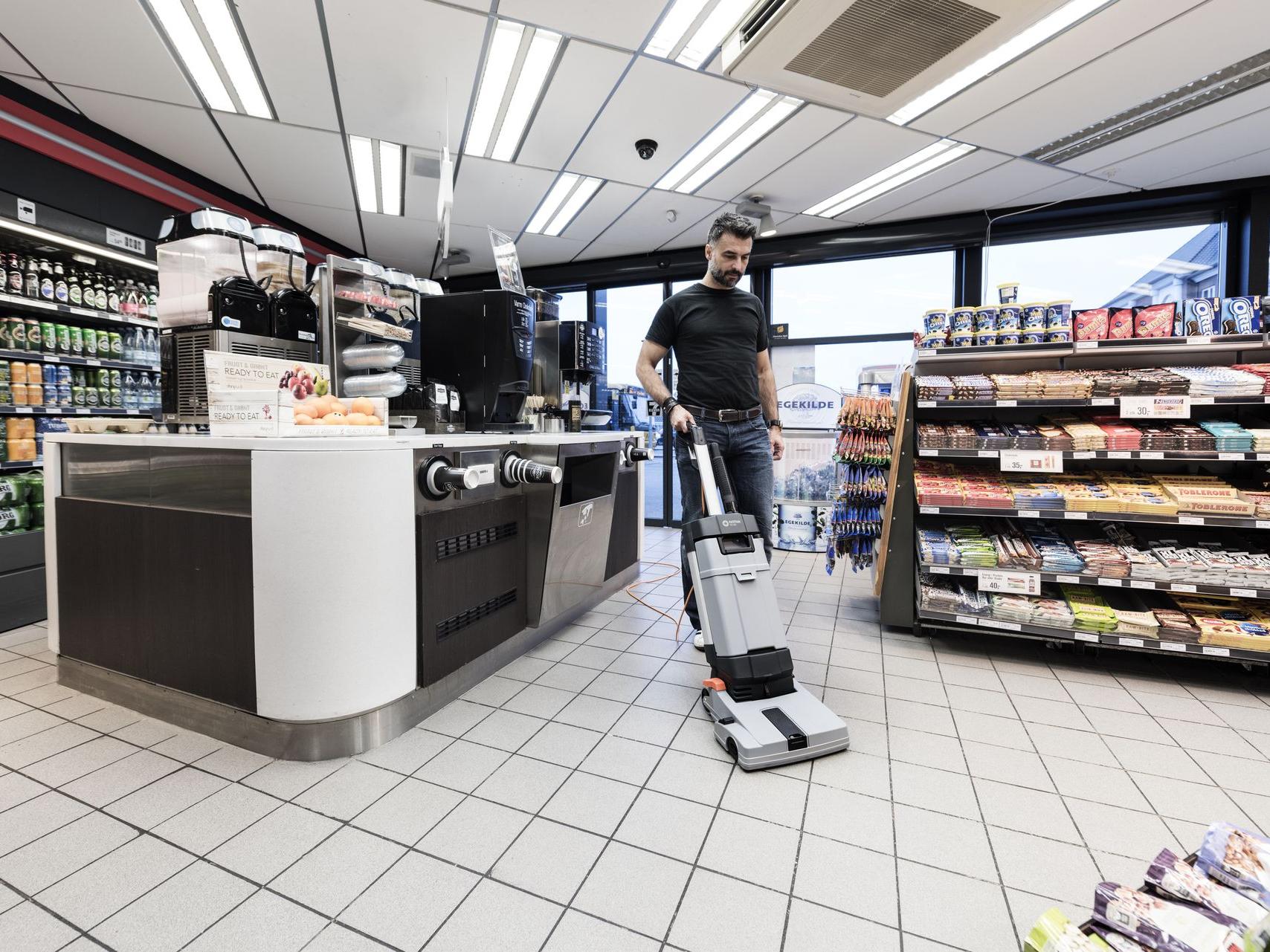 Floor scrubber cleaning supermarket aisles in a busy retail environment.
