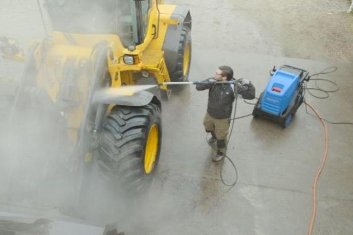 Worker cleaning around heavy machinery using site-maintenance equipment to manage dust and debris in mining areas